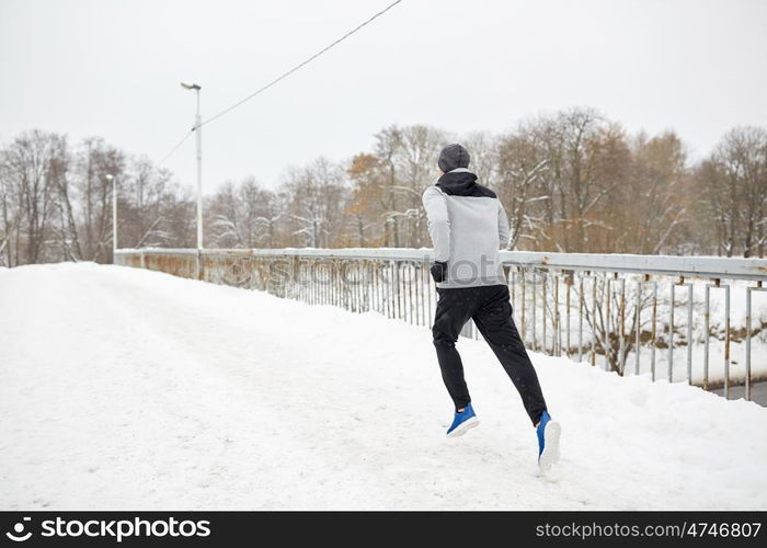 fitness, sport, people, season and healthy lifestyle concept - young man running along snow covered winter bridge road