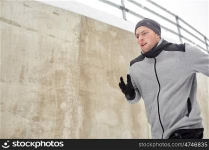 fitness, sport, people, season and healthy lifestyle concept - young man running along concrete wall in winter