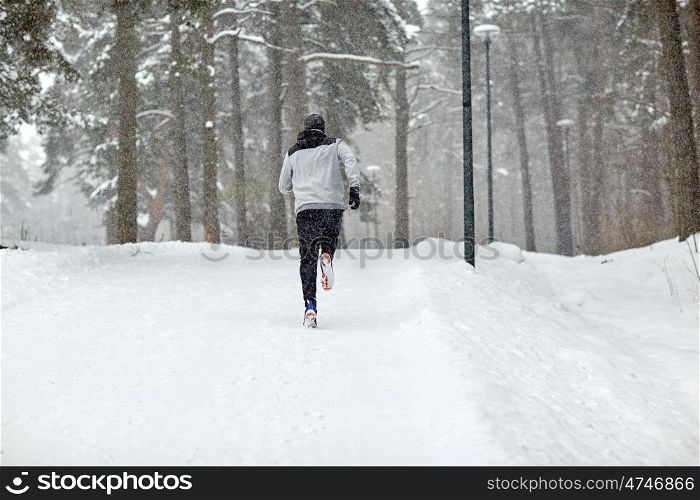 fitness, sport, people, season and healthy lifestyle concept - young man running on snow covered winter road in forest