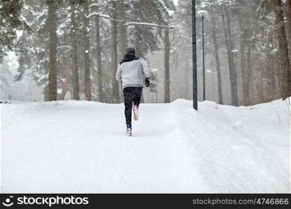 fitness, sport, people, season and healthy lifestyle concept - young man running on snow covered winter road in forest