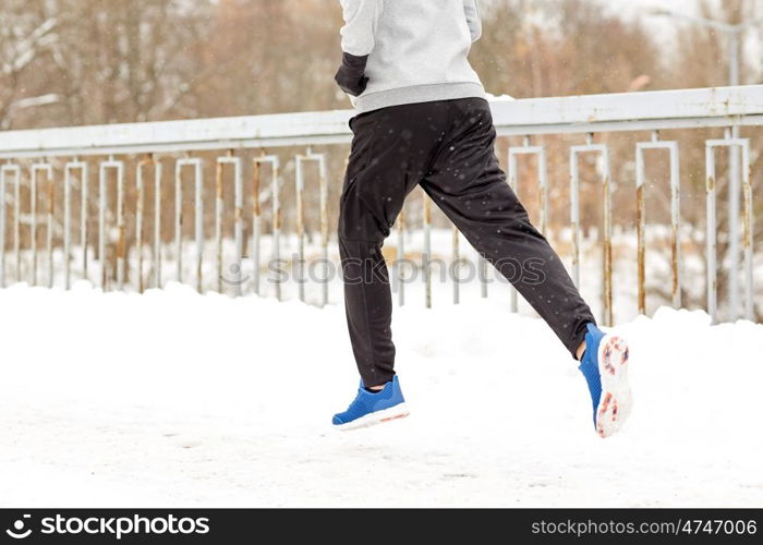 fitness, sport, people, season and healthy lifestyle concept - young man running along snow covered winter bridge road