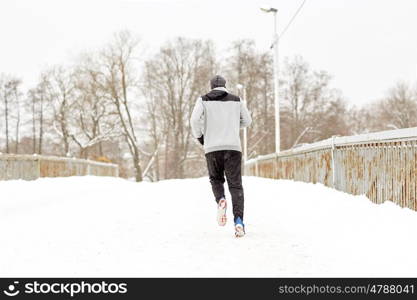 fitness, sport, people, season and healthy lifestyle concept - young man running along snow covered winter bridge road