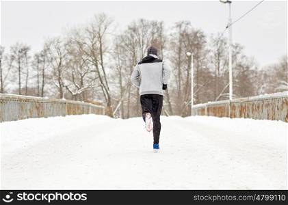 fitness, sport, people, season and healthy lifestyle concept - young man running along snow covered winter bridge road
