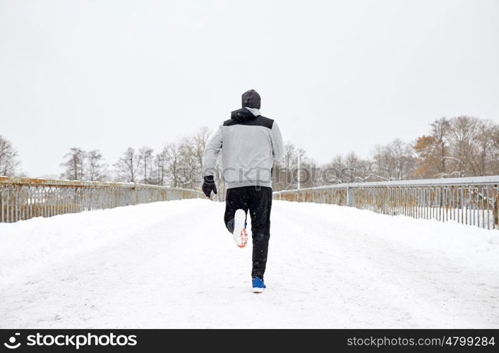 fitness, sport, people, season and healthy lifestyle concept - young man running along snow covered winter bridge road