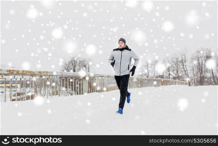 fitness, sport, people, season and healthy lifestyle concept - young man running along snow covered winter bridge road. man running along snow covered winter bridge road