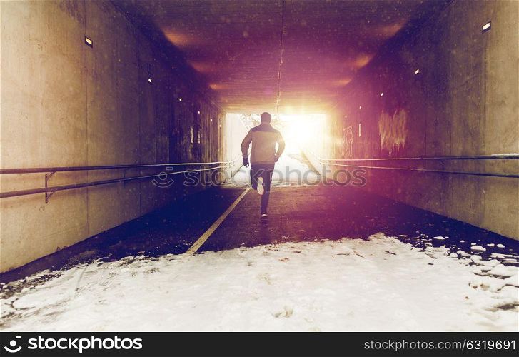 fitness, sport, people, season and healthy lifestyle concept - young man running along pedestrian subway tunnel in winter. man running along subway tunnel in winter