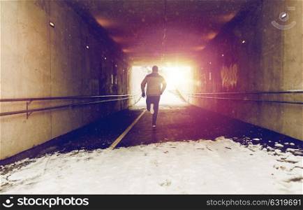 fitness, sport, people, season and healthy lifestyle concept - young man running along pedestrian subway tunnel in winter. man running along subway tunnel in winter