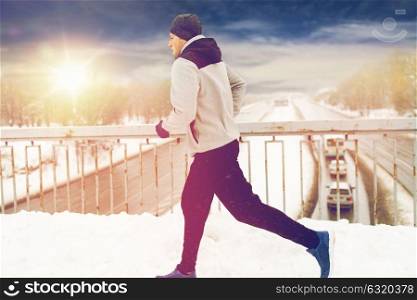 fitness, sport, people, season and healthy lifestyle concept - young man running along snow covered winter bridge road. man running along snow covered winter bridge road