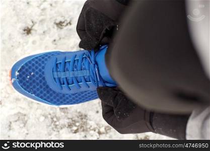 fitness, sport, people, sportswear and footwear concept - close up of man foot and hands tying shoe lace in winter outdoors