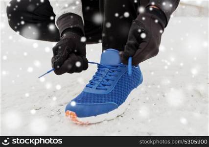 fitness, sport, people, sportswear and footwear concept - close up of man foot and hands tying shoe lace in winter outdoors. close up of man tying shoe lace in winter outdoors