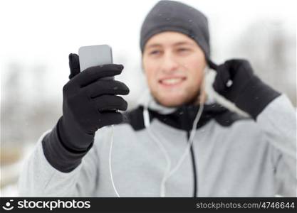 fitness, sport, people, technology and healthy lifestyle concept - close up of happy smiling young man in earphones with smartphone listening to music in winter