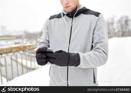 fitness, sport, people, technology and healthy lifestyle concept - close up of young man in earphones with smartphone listening to music on winter bridge