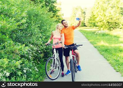 fitness, sport, people, technology and healthy lifestyle concept - happy couple with bicycle taking taking selfie by smartphone outdoors
