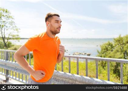 fitness, sport, people, technology and healthy lifestyle concept - happy man with earphones running outdoors