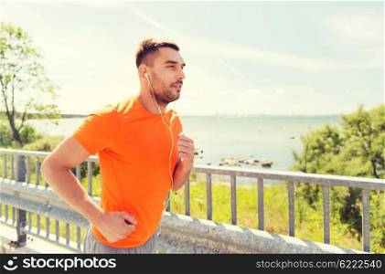 fitness, sport, people, technology and healthy lifestyle concept - happy man with earphones running outdoors