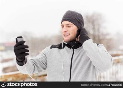fitness, sport, people, technology and healthy lifestyle concept - happy smiling young man in earphones with smartphone listening to music on winter bridge