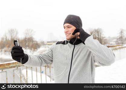 fitness, sport, people, technology and healthy lifestyle concept - happy smiling young man in earphones with smartphone listening to music on winter bridge