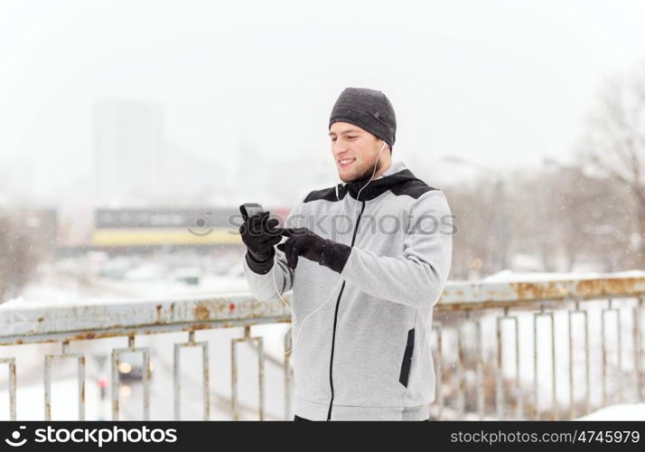 fitness, sport, people, technology and healthy lifestyle concept - happy smiling young man in earphones with smartphone listening to music on winter bridge