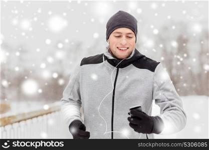 fitness, sport, people, technology and healthy lifestyle concept - happy young man in earphones with smartphone listening to music and running along winter road. happy man with earphones and smartphone in winter