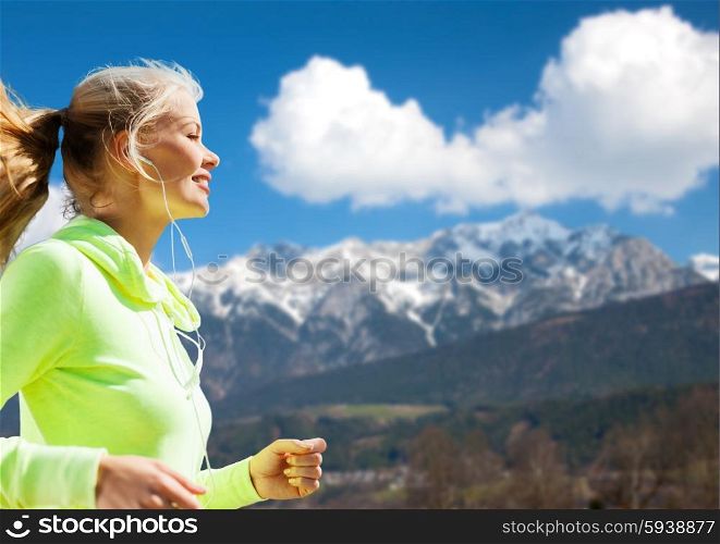 fitness, sport, people, technology and healthy lifestyle concept - happy young woman with earphones jogging over mountains and blue sky background