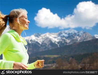 fitness, sport, people, technology and healthy lifestyle concept - happy young woman with earphones jogging over mountains and blue sky background