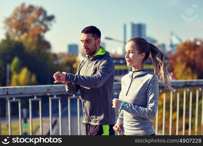 fitness, sport, people, technology and healthy lifestyle concept - smiling couple with heart-rate watch running over city highway bridge. couple running over city highway bridge