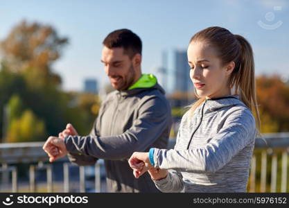 fitness, sport, people, technology and healthy lifestyle concept - smiling couple with heart-rate watch running over city highway bridge