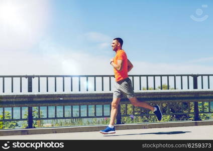 fitness, sport, people, technology and healthy lifestyle concept - smiling young man with heart rate watch running at summer seaside