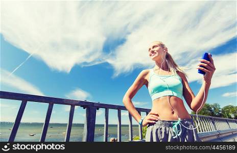 fitness, sport, people, technology and healthy lifestyle concept - smiling young woman with smartphone and earphones listening to music and exercising outdoors