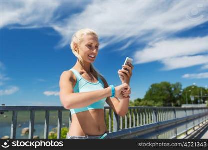 fitness, sport, people, technology and healthy lifestyle concept - smiling young woman with heart rate watch and smartphone exercising outdoors