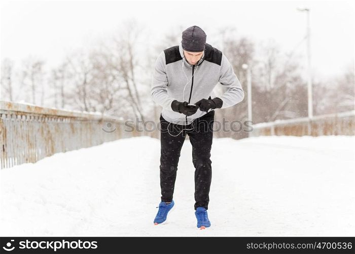 fitness, sport, people, technology and healthy lifestyle concept - young man in earphones with smartphone listening to music and running along winter road