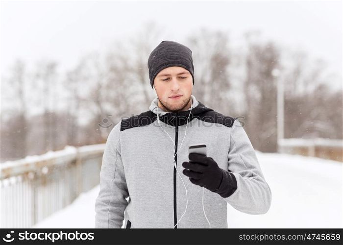 fitness, sport, people, technology and healthy lifestyle concept - young man in earphones with smartphone listening to music on winter bridge