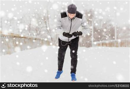 fitness, sport, people, technology and healthy lifestyle concept - young man in earphones with smartphone listening to music and running along winter road. man with earphones and cellphone running in winter