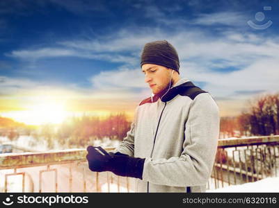 fitness, sport, people, technology and healthy lifestyle concept - young man in earphones with smartphone listening to music on winter bridge. man in earphones with smartphone on winter bridge