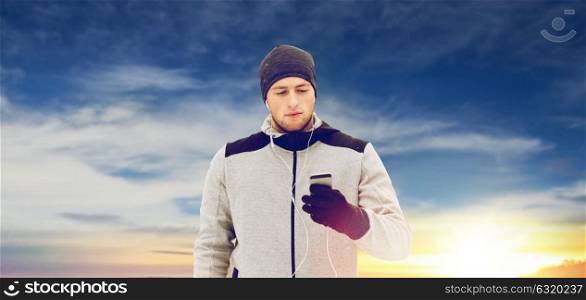 fitness, sport, people, technology and healthy lifestyle concept - young man in earphones with smartphone listening to music on winter bridge. happy man with earphones and smartphone in winter