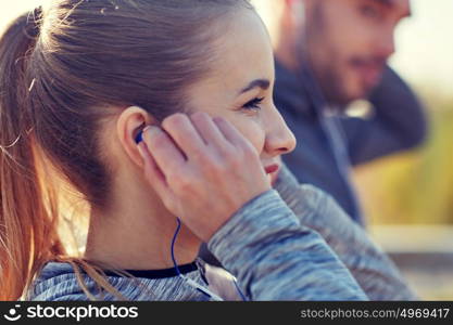 fitness, sport, people, technology and lifestyle concept - happy couple outdoors and listening to music in earphones. happy woman with earphones listening to music