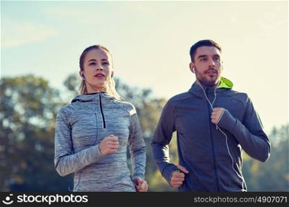 fitness, sport, people, technology and lifestyle concept - happy couple running and listening to music in earphones outdoors. happy couple with earphones running outdoors