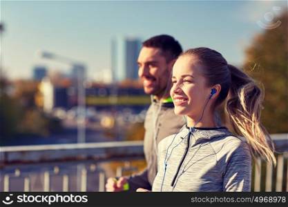 fitness, sport, people, technology and lifestyle concept - happy couple running and listening to music in earphones at city. happy couple with earphones running in city