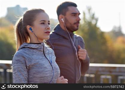 fitness, sport, people, technology and lifestyle concept - happy couple running and listening to music in earphones at city
