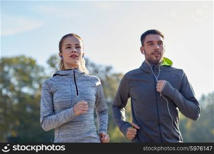 fitness, sport, people, technology and lifestyle concept - happy couple running and listening to music in earphones outdoors