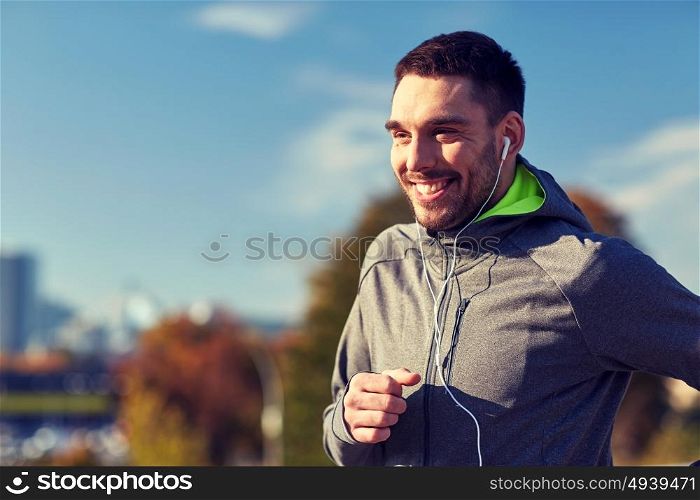 fitness, sport, people, technology and lifestyle concept - happy man running and listening to music in earphones at city. happy man with earphones running in city