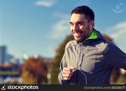 fitness, sport, people, technology and lifestyle concept - happy man running and listening to music in earphones at city. happy man with earphones running in city