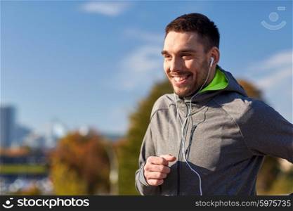 fitness, sport, people, technology and lifestyle concept - happy man running and listening to music in earphones at city