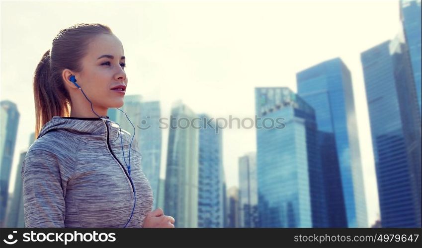 fitness, sport, people, technology and lifestyle concept - happy woman running and listening to music in earphones over singapore city skyscrapers background. happy woman with earphones running in city