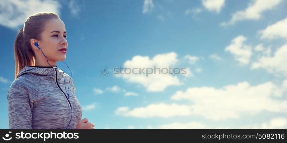 fitness, sport, people, technology and lifestyle concept - happy woman running and listening to music in earphones over blue sky and clouds background. happy woman with earphones running over blue sky