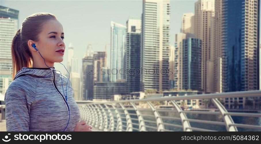 fitness, sport, people, technology and lifestyle concept - happy woman running and listening to music in earphones over dubai city street background. happy woman with earphones running over dubai city. happy woman with earphones running over dubai city