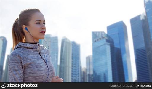 fitness, sport, people, technology and lifestyle concept - happy woman running and listening to music in earphones over singapore city skyscrapers background