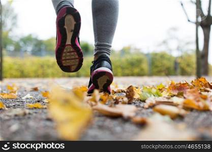 fitness, sport, people, wear and healthy lifestyle concept - close up of young woman running in autumn park