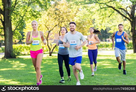 fitness, sport, race and healthy lifestyle concept - group of happy people or sportsmen running marathon with badge numbers at summer park. happy young sportsmen racing wit badge numbers