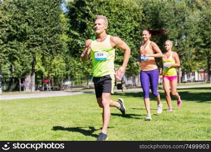 fitness, sport, race and healthy lifestyle concept - group of happy people or sportsmen running marathon with badge numbers at summer park. happy young sportsmen racing wit badge numbers